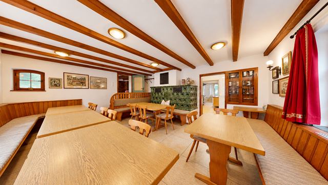 Allgäustube der Ruhmühle mit langen Tischen, Sitzbänken und grünem Kachelofen